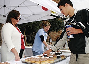 Brenda Keagle, left, and Stephanie Cunningham from the Directors Advisory Group help classics senior Buddy Lopez and other passersby students on the Mall pick free cupcakes yesterday afternoon, baked and served in honor of the Student Union Memorial Centers 56th birthday.