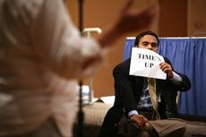 Chris Gustafson, an intern for Senate Democrats, holds a sign signaling the speaker has reached the conclusion of her three minute time limit during the Democratic Public Hearing held in the South Ballroom of the SUMC Thursday night.