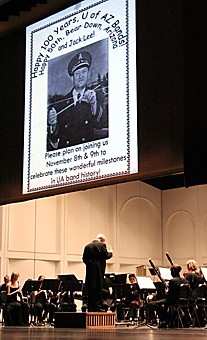A projection of Jack Lee, former band leader and composer of the Bear Down, Arizona fight song, hangs above the UA Wind Ensemble yesterday afternoon at a memorial concert honoring the legendary director. Lee led the university bands for more than 30 years, developing innovative marching techniques and directing the band during its performance in the first Super Bowl.