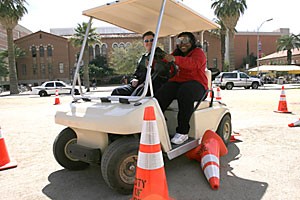 Wearing goggles that simulate drunken vision, criminal justice sophomore Gybrielle Demaree plows a cone while running the drunken golf cart obstacle course with Tucson Police Department Officer Corie Nolan yesterday afternoon during an event on the UA Mall. The event was held so that police could advise students on proper and safe behavior for spring break.
