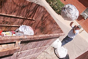Custodial worker Tomas Gonzalez tosses some trash near Graham-Greenlee Residence Hall yesterday. Dumpster diving may become a problem as students throw away items in preparation of moving out.