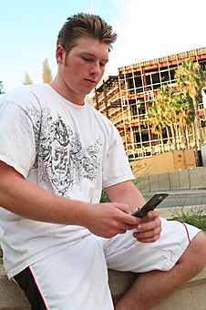 Justin Fritch, a pre-architecture sophomore takes a break to use his cell phone while he works on his architecture homework in front of the Park Student Union yesterday afternoon. ASUA has signed a contract with Mobile Campus that will allow professors to text. 