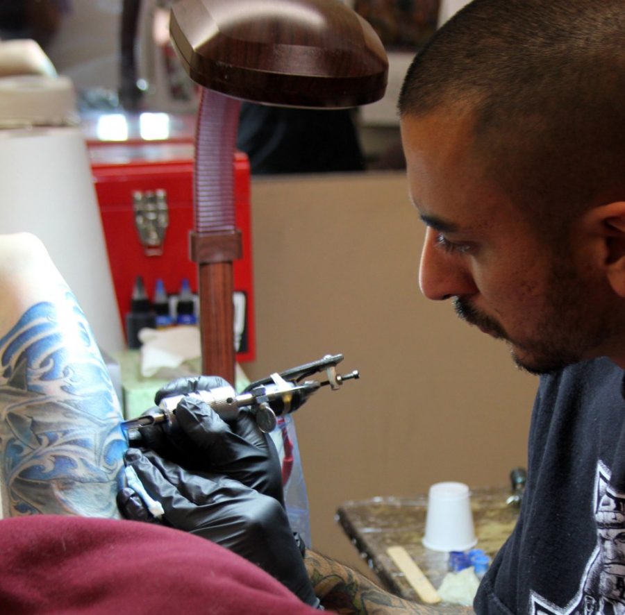 Rebecca Marie Sasnett / The Daily Wildcat

Xavier Morales, tattoo artists at Ancient Art Tattoo for 2 and a half years, colors in Pima student Kelbee Smith's dolphin and shark tattoo at Ancient Art Tattoo on Tuesday, Nov. 18, 2014. Morales has been a tattoo artist for 6 years.