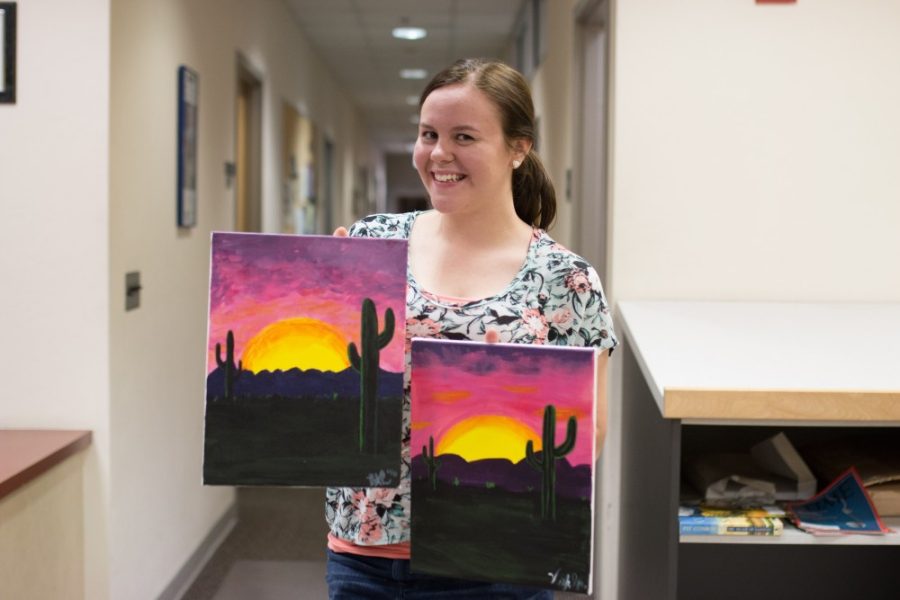 Rebecca Reiter poses with a friends painting and her own that they created at Mocktails with Monet. The event walked students through step-by-step instructions to create their own masterpieces.