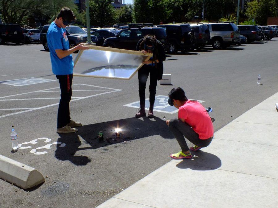 Two volunteers use a large Fresnel lens to direct the light from the sun to a focused point, creating energy to melt pennies. The Fresnel lens and many other hands-on activities were avilable to teach kids about science at last weekend's Laser Fun Day