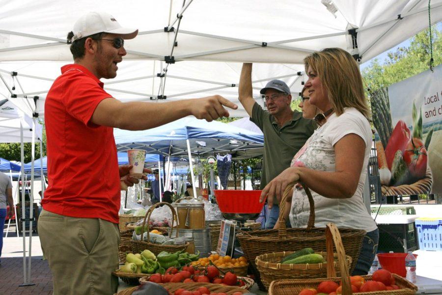 Clayton Kammerer, left, chats with Cindy Williams, right, at her produce stand, Cindy Gardens, during the weekly farmers market at St. Philips Plaza in Tucson, Ariz. on Sunday, July 10, 2016. Cindy Gardens has been in business for six months and has been working the farmers market at St. Philips Plaza for five months.