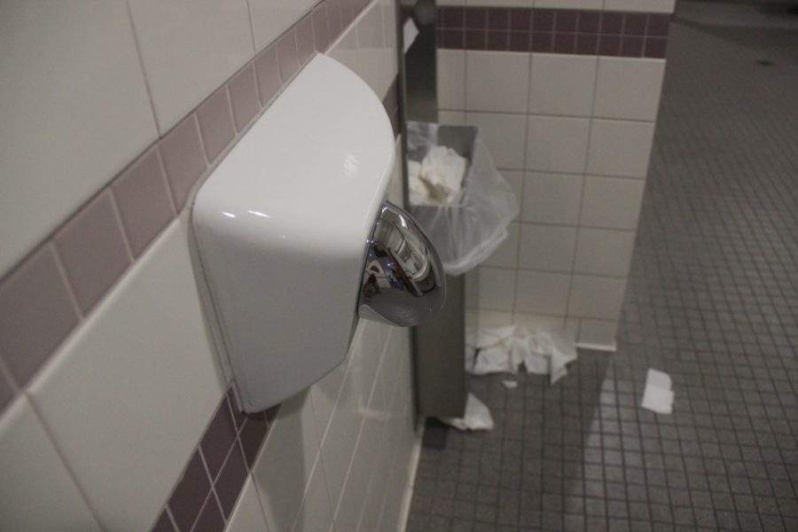 A hand dryer inside the University Services Building sits high above the trash created by paper towels.
