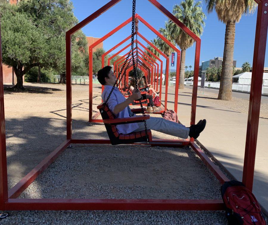 Joseph Siml, a University of Arizona junior majoring in architecture, on the red swings that are part of the Arizona Arts Live installation, “Mi Casa, Your Casa 2.0.” The swings will be in front of the Modern Languages building until Nov. 7.