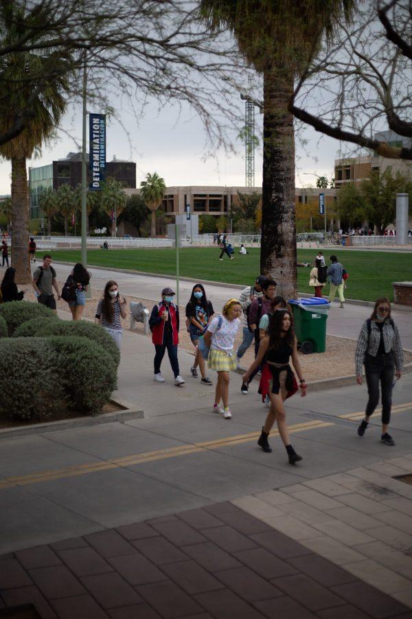 A group of students, some in masks, walk down the sidewalk of the UA Mall. 