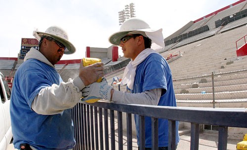 Jose Flores, left, and Cresencio Ramos work together moving materials across a fence for patching the concrete steps of the UA football stadium yesterday. The workers will be patching and repairing only the west side, middle step of the stadium.