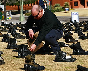 Jim Strader, an Episcopalian minister at the Campus Christian Center, reads the name and age of a fallen soldier tagged on a pair of boots Friday on the UA Mall. The Chicago-based American Friends Service Committee displayed the exhibit Eyes Wide Open, a collection of combat boots and shoes that represent lives lost in Iraq, both military and civilian.