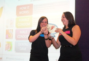 Shannon Quay and Alyssa Padilla, health and sexuality interns for the Womens Resource Center, demonstrate the proper use of various condoms at the Sex Ed Presentation on Thursday night. The event was sponsored by Womens Resource Center, Campus Health and Planned Parenthood of Arizona. 
