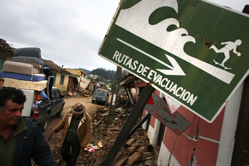 Residents in Constitucion, Chile, pass a sign pointing to an evacuation route in the event of a tsunami on Monday, March 1, 2010. A massive 8.8 earthquake struck the area on Saturday. (Michael Robinson Chavez/Los Angeles Times/MCT)