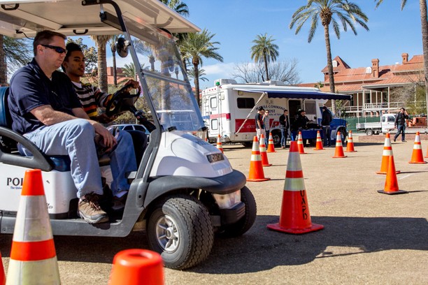 Noelle Haro-Gomez/Arizona Daily Wildcat
From the left, Scott Sullivan an officer with Tucson Police Department, rides in the police golf cart  while a UA student, Perris Howard, Sophomore, drives in the impared similation driving course at the UA Spring Break Safety Fair. Students are given googles that distorts their vision to give them the idea of how it is to drive drunk.