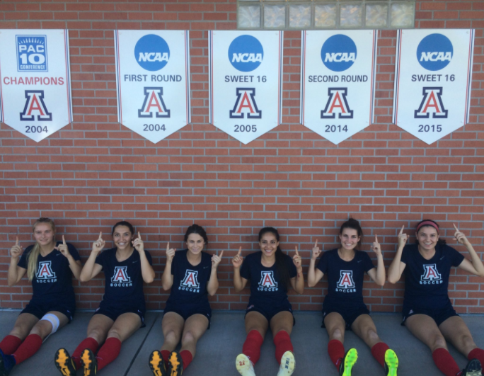 Members of Arizona soccers senior class point at the programs NCAA Tournament banners. From left to right: Haley Silverberg, Lexe Selman Richards, Paige Crouch, Laura Pimienta, Jaden DeGracie-Bailey, and Hannah Stevens