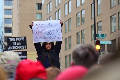 A protestor holds a sign reading "you will reap what you have sown" as Trump supporters file out of the inauguration of President Donald Trump in Washington D.C. on Friday, Jan. 20, 2017. Shortly after this moment, a Trump supporter nabbed the sign from the protestor and refused to return it. (Photograph by Rebecca Noble)