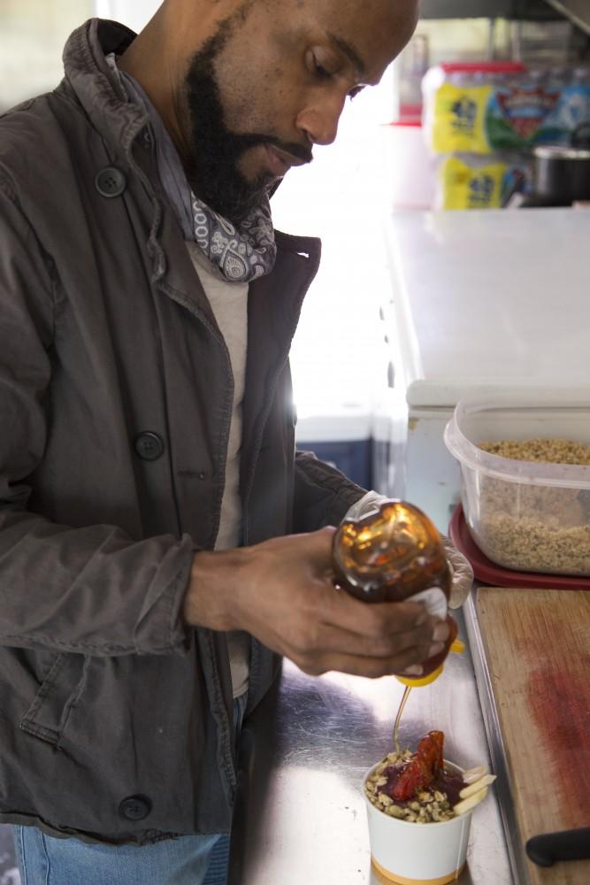 Co-owner André Newman pours honey onto an açaí bowl in his food truck called Purple Tree Organic Açaí Blends. 