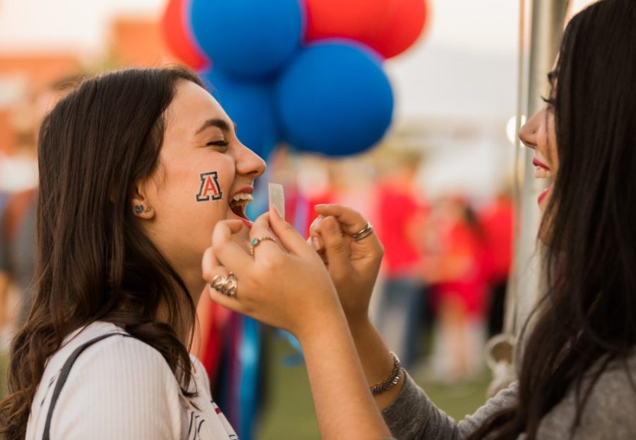 Two UA alums laugh while putting on fake Arizona tattoos during homecoming last year.