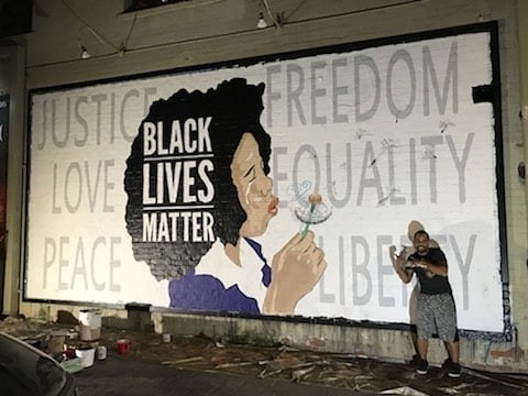  Robbie Lee Harris stands with his mural on the side of the Rialto Theater. (Photo courtesy Robbie Lee Harris) 