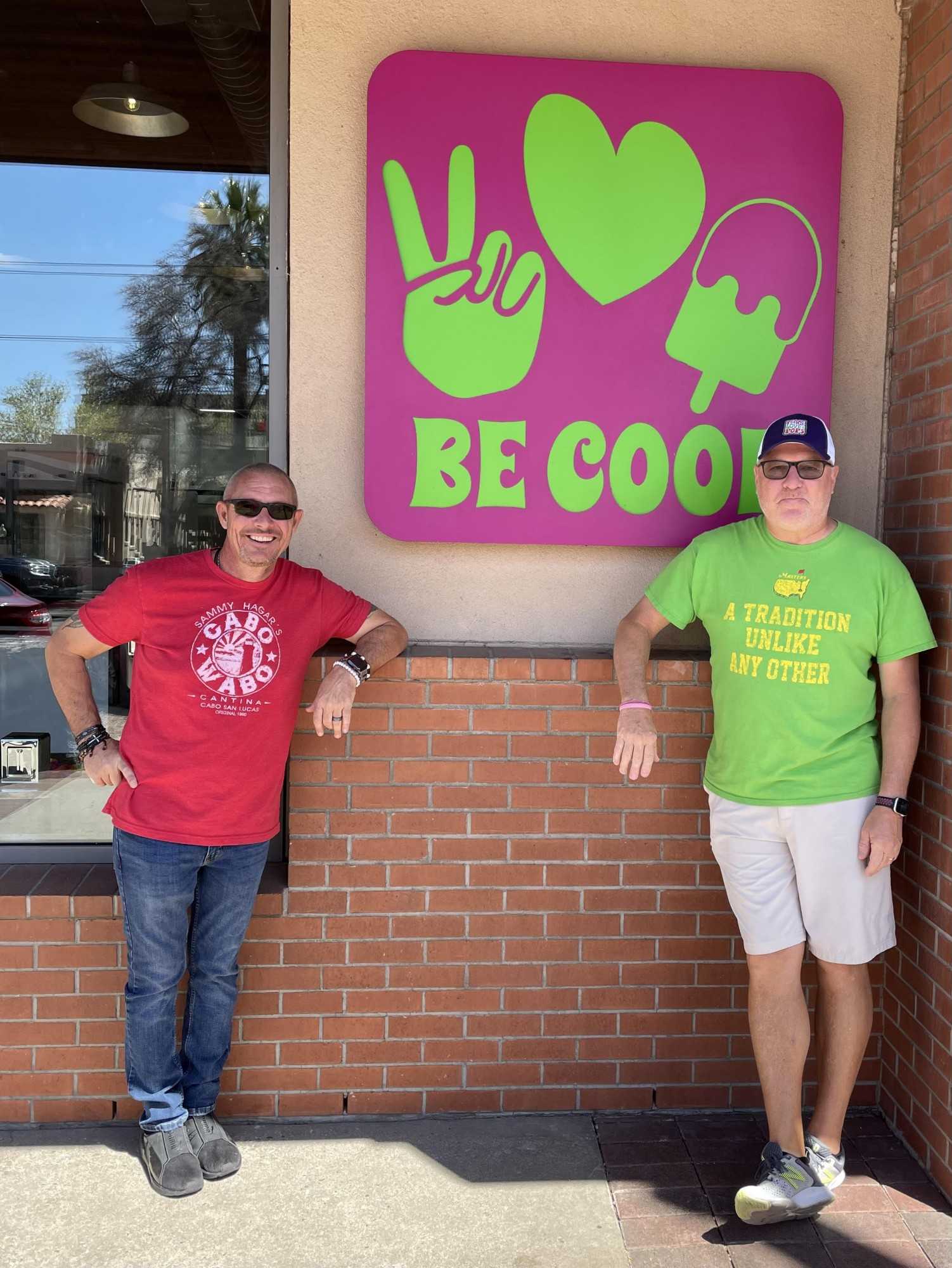 Peace, Love & Pops owners Jim Roberts, left, and Scot Harrison, right, stand in front of a sign outside of their business.