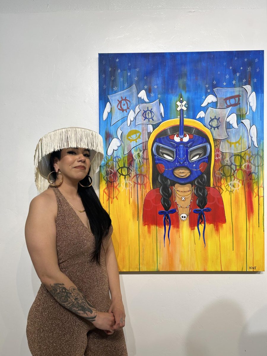 Cynthia Naugle posing with a painting featured in &gallery’s second-anniversary celebration exhibit. The theme was “&,” and featured a variety of works. 