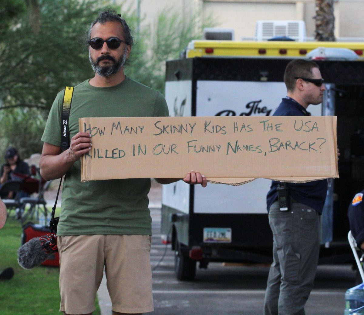 A man stands and holds a sign outside the Obama rally on Oct. 18. The sign reads, "How many skinny kids has the USA killed in our funny names, Barack?"